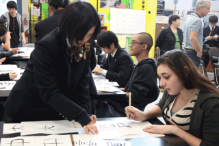 A student from Takata High teaches a Del Norte student the basics of writing kanji